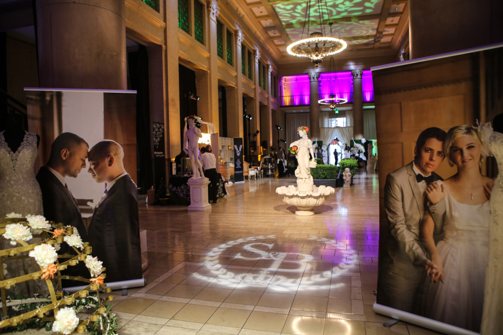 Wedding decor and photos set-up with married couple's initials projected on the floor infant of indoor fountain statue inside venue and ambient chandelier lights 