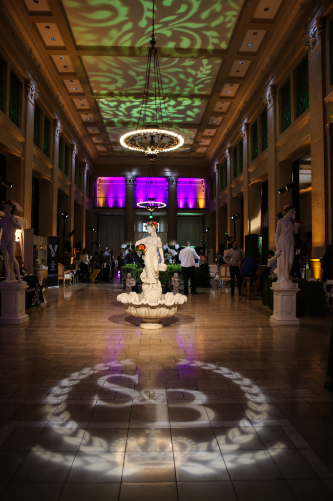 Wedding venue decorum of fountain statues, chandelier lights, pattern wash lights on the ceiling, multicolored lights and the wedding couple's initials projected onto the floor
