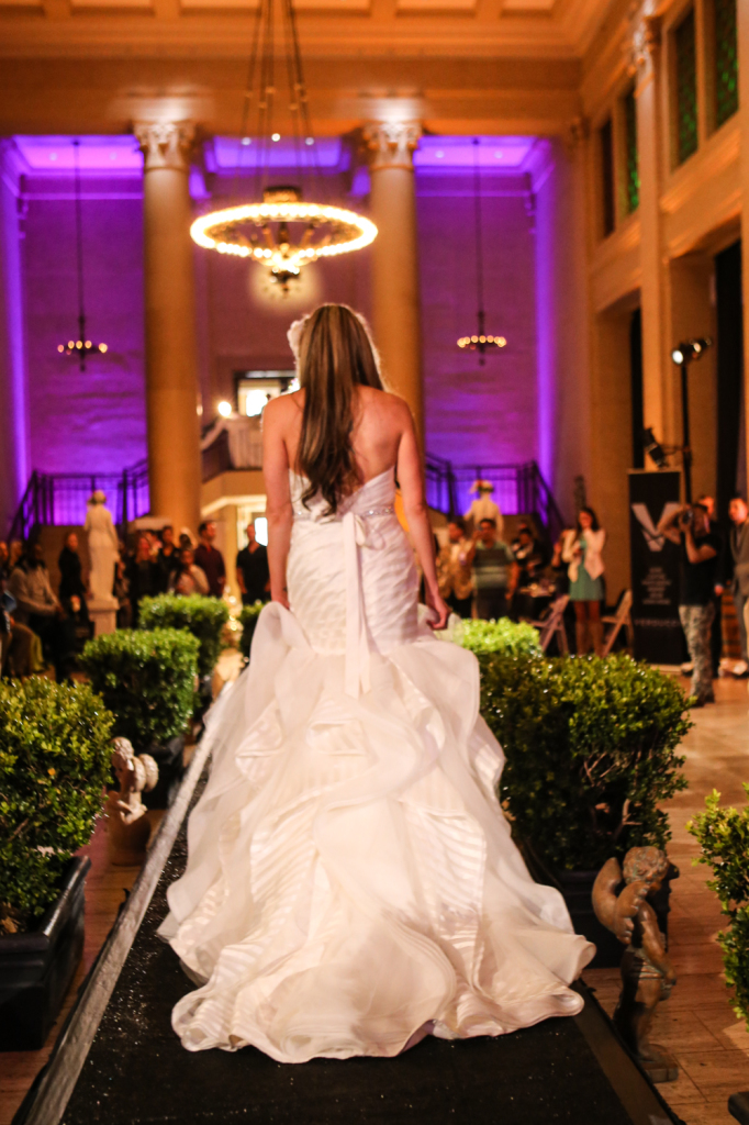 Bride model on runway for vanity wedding show with purple wall lighting in background and chandelier lights