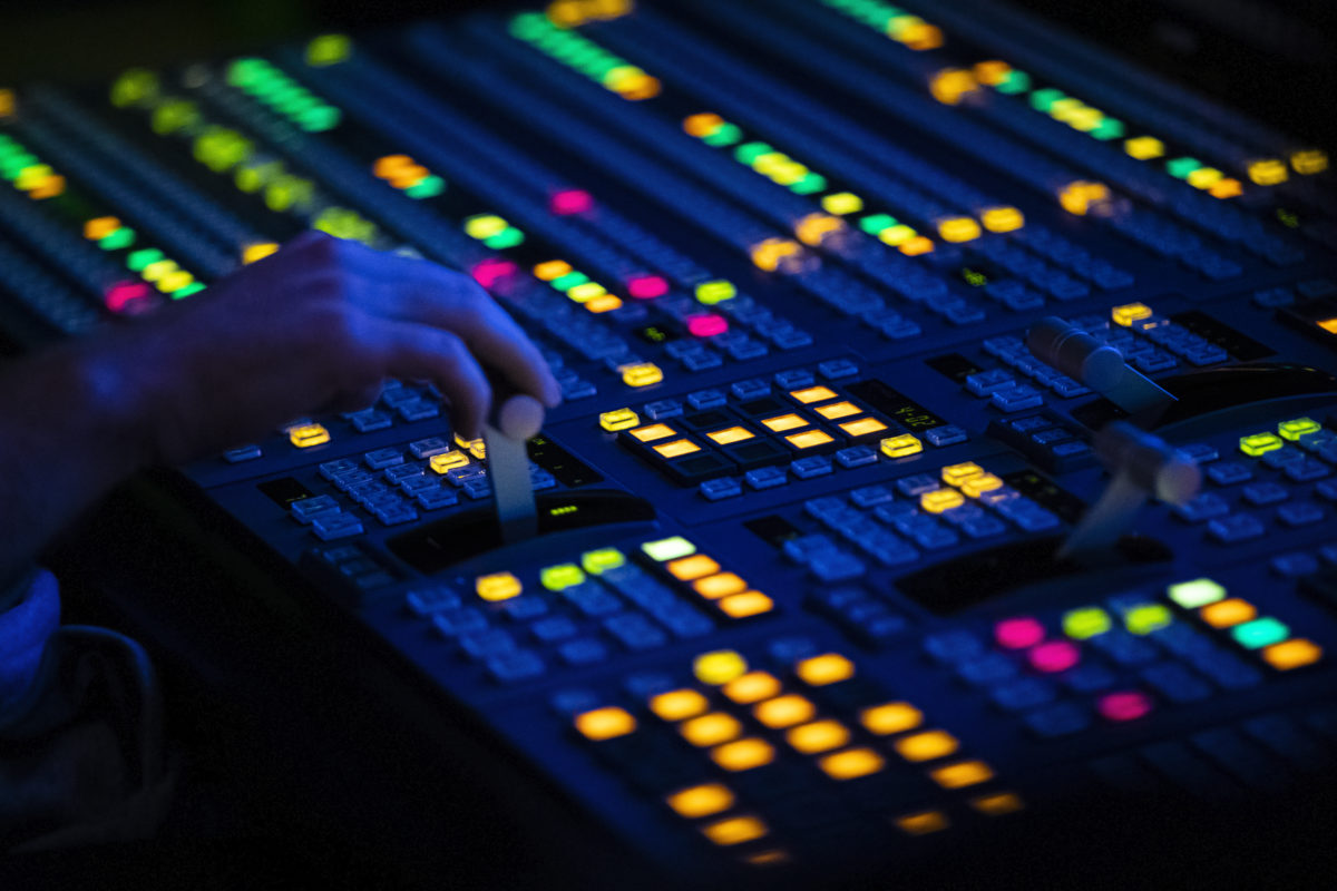 virtual events - Close Up of a Video Control Switcher Board with brightlyColored Lights in a dark control room in a media center
