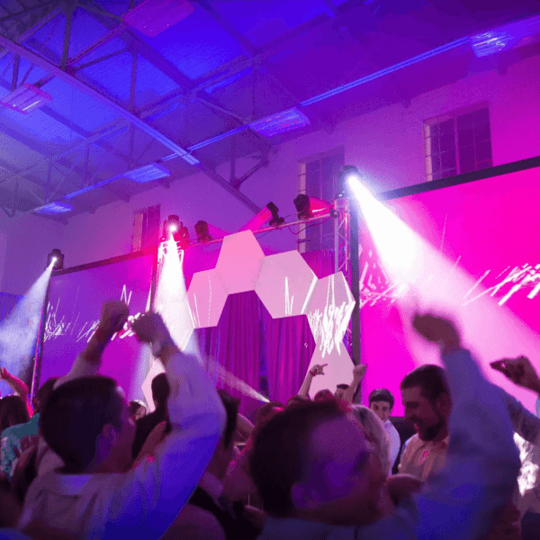 People dancing on the dance floor in front of the DJ booth stage with purple spot lights and a screen projector