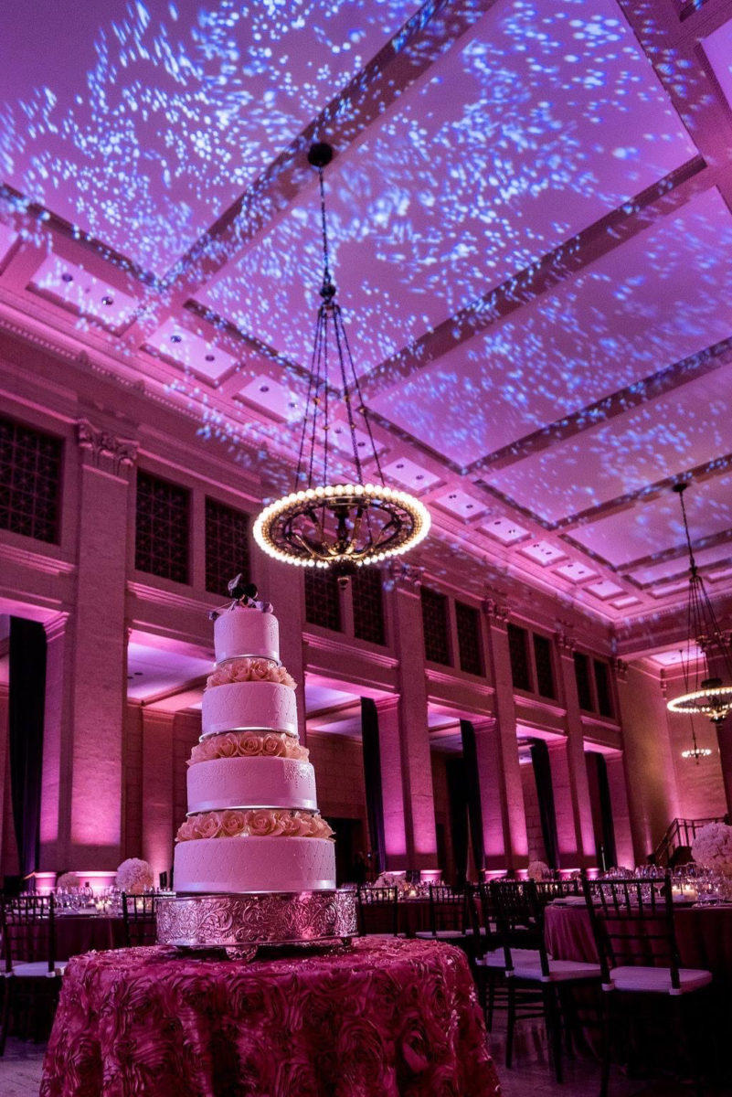 Wedding cake lighting and placement with multicolored venue lights and ceiling pattern wash