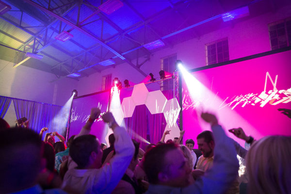 Wedding crowd dancing under multicolored lights with a digital screen on wedding dance floor